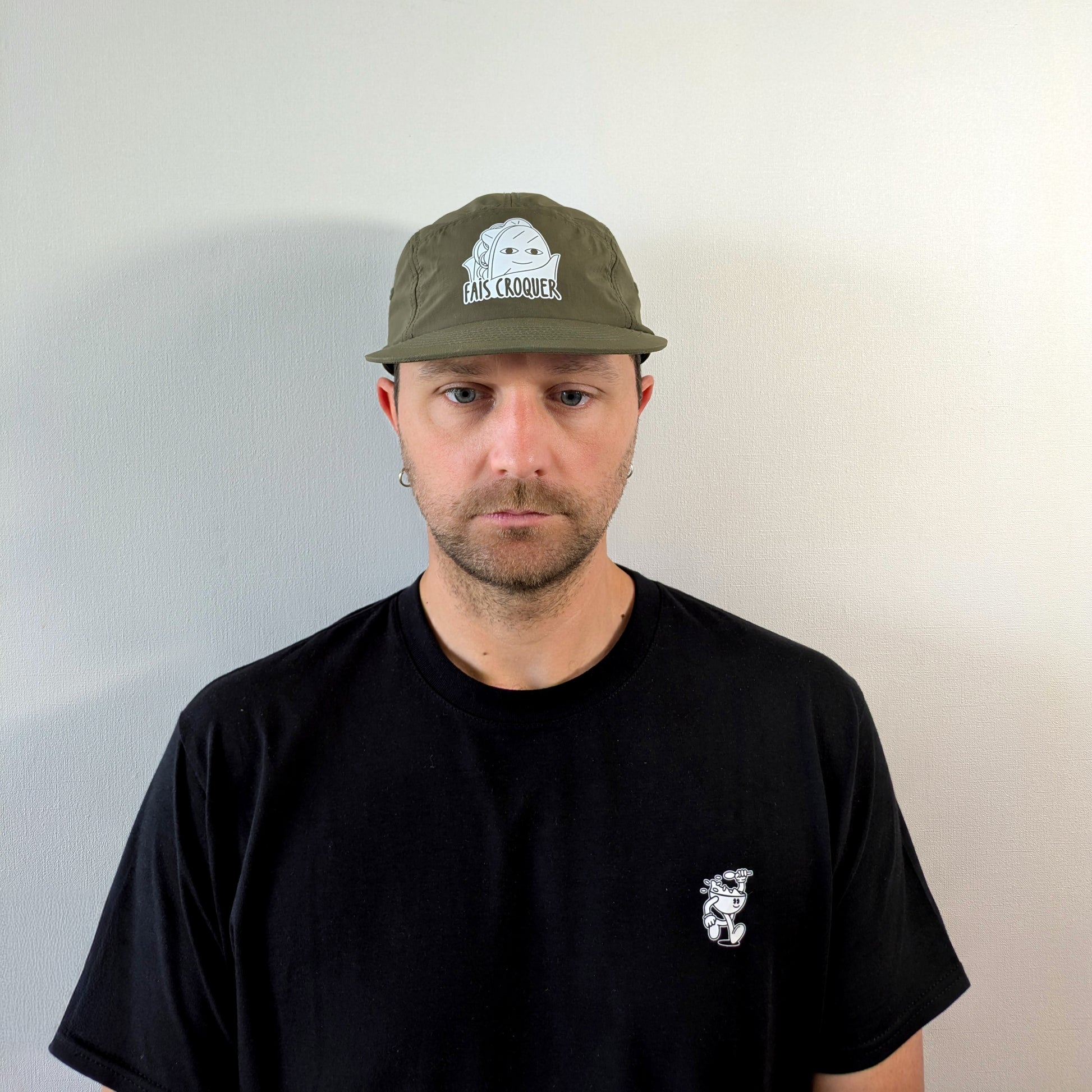 Homme portant la casquette verte Fais Croquer, style minimaliste avec t-shirt noir illustré